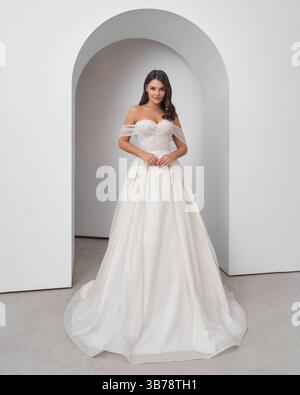 Brünette Frau im Hochzeitskleid posiert anmutig in heller Inneneinrichtung Stockfoto