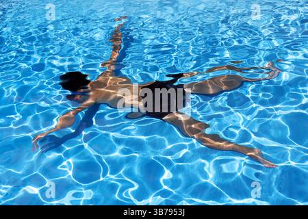 Mann schwimmt unter Wasser mit leichten Wellen, die sich im blauen Wasser des Schwimmbades spiegeln Stockfoto