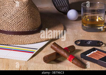 Siesta: Zigarre, Strohhut, Scotch Whiskey und Golffahrer auf einem Holztisch Stockfoto