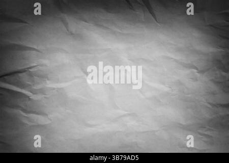 Graues zerknittertes Papier sorgt für einen strukturierten Hintergrund, beleuchtet durch dramatische Beleuchtung und schafft eine abstrakte und stimmungsvolle Atmosphäre Stockfoto