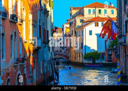 Malerischer Kanal in Venedig, gesäumt von farbenfrohen Gebäuden mit Bogenfenstern und Balkonen, die in warmes Sonnenlicht getaucht sind. Kleine Brückenbögen über t Stockfoto