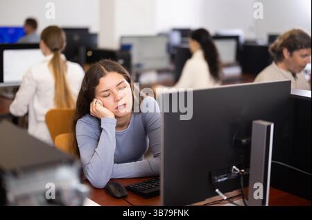 Junge Studentin schläft während der Fortbildung im Computerlabor ein Stockfoto