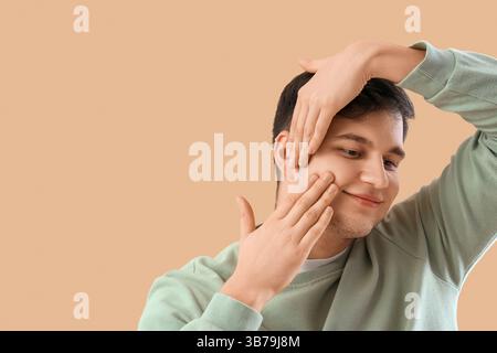 Junger Mann, der Gesichtsaufbauübung auf beigefarbenem Hintergrund macht Stockfoto