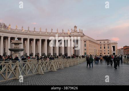 Petersplatz bei Sonnenuntergang während der Weihnachtszeit mit geschmückten Pilgermassen und sanftem pastellfarbenem Himmel um die Kolonnaden der Vatikanstadt. Hochwertige Fotos Stockfoto