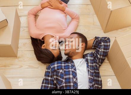 Oben Ansicht des jungen schwarzen Kerls und seiner Freundin, die auf dem Boden zwischen den Kartons liegen und einander an bewegenden Tag betrachten Stockfoto