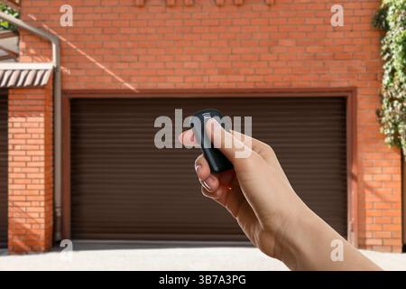 Frau, die die Garagentür draußen mit Fernbedienung steuert, Nahaufnahme Stockfoto