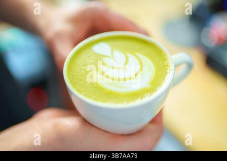 Barista hält eine Tasse Matcha Latte in den Händen Stockfoto
