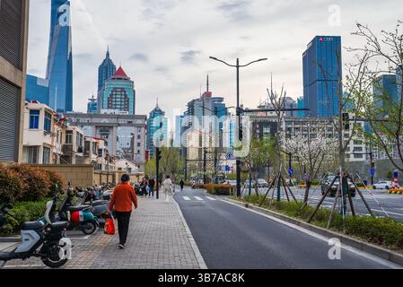 Shanghai, China - 1. April 2025: Abend im Stadtteil Pudong mit Sonnenuntergang. Blühende Frühlingsbäume und moderne Wolkenkratzer. Chinesische Fußgänger walki Stockfoto