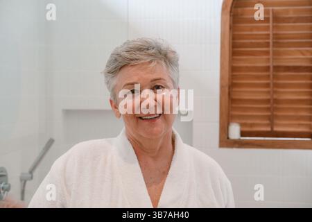 Eine ältere Frau steht im Badezimmer vor dem Spiegel mit feuchtigkeitsspendenden Flecken Stockfoto