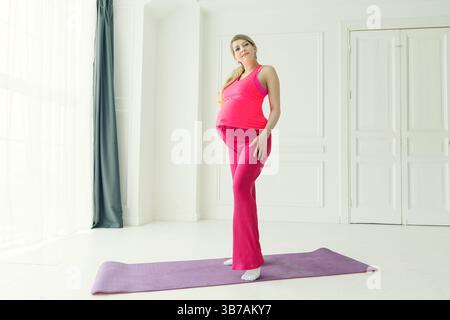 Eine schwangere Frau mit Bauch steht auf einer Matte und bereitet sich auf Übungen vor Stockfoto