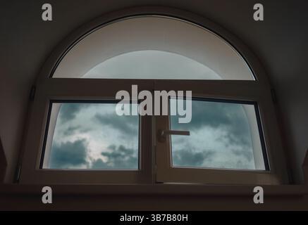 Interessantes halbrunde Fenster mit offenem rechten Flügel, Dachboden tagsüber. Stockfoto