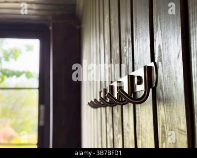 Eine Nahaufnahme eines verchromten Wandhakens, der an einer gekachelten Wand montiert ist. Die reflektierende Metalloberfläche fängt Licht ein und betont sein elegantes und elegantes Design Stockfoto
