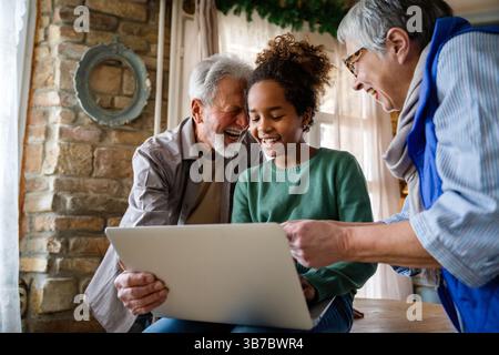 Glückliches Seniorenpaar, das mit einem modernen Computer-Laptop zusammen mit dem Enkel zu Hause arbeitet. Stockfoto