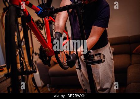Man in Handschuhen strafft die Kurbelgarnitur an rotem Motorrad mit Werkzeugen in einer gemütlichen Innenumgebung, die sich auf präzise Wartung konzentriert. Stockfoto