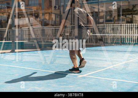 Mann, der Padel auf einem blauen Hof in Marbella spielt, spiegelt sich in der urbanen Glassportkultur Südspaniens wider Stockfoto