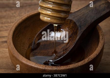 Honig tropft aus einem Löffel in einer Holzschale mit einem Holzlöffel Stockfoto