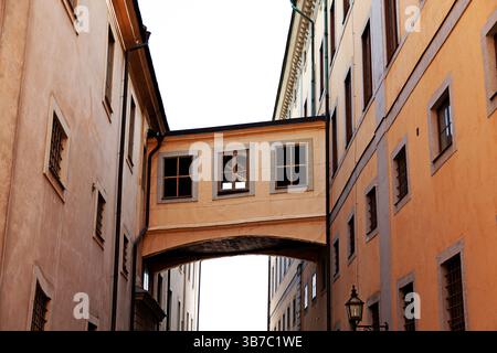 A narrow alleyway between warm terracotta-colored buildings in a European city, featuring an architectural sky bridge connecting the structures and a Stockfoto
