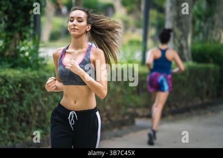 Zielgerichtete junge Frau, die während des Sommertrainings in einem Stadtpark joggt, Sportbekleidung trägt und einen aktiven Lebensstil genießt. Stockfoto