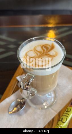 Eleganter Cappuccino mit komplizierter Latte Art in einem klaren Glas auf Holztablett fängt Gelassenheit und Raffinesse bei jedem Schluck ein. Stockfoto