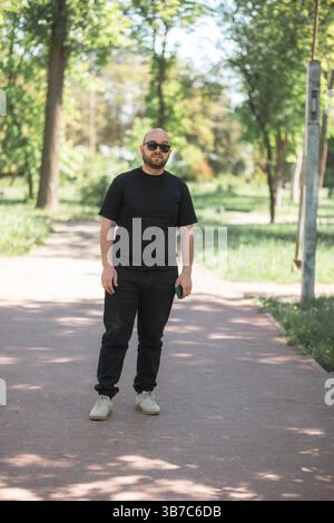 Stehendes Porträt eines Mannes in lässiger Kleidung mit Sonnenbrille. Das Foto wurde im Park gemacht. Stockfoto