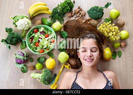 Junge Frau umgeben von frischem Gemüse und Obst. Eine junge Frau, die mit geschlossenen Augen auf dem Boden liegt, umgeben von einer Reihe frischer Stockfoto