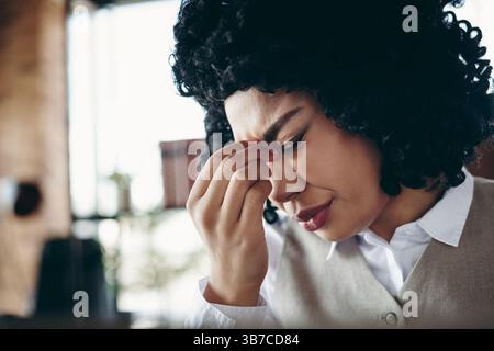Professionelle Geschäftsfrau, die an ihrem Arbeitsplatz müde wird, spiegelt Hingabe und Engagement für ihre Karriere wider Stockfoto