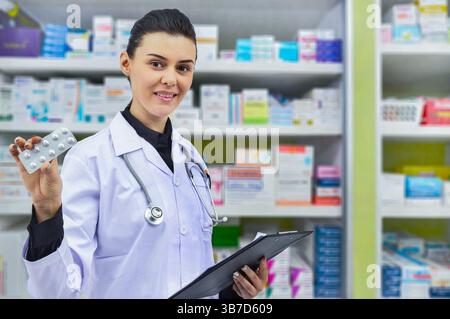 Schöne junge Apothekerin mit Medikamentenkapsel und Verordnungstabelle zum Abfüllen von Rezepten in Apotheken-Drogerien Stockfoto
