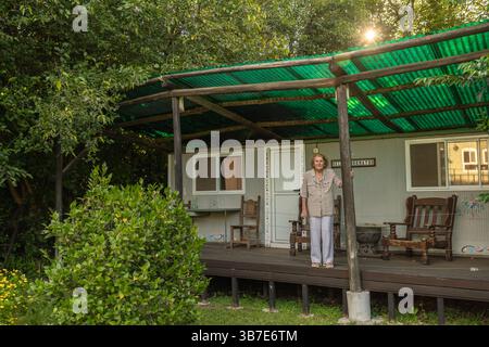 Seniorin genießt Ruhestand in einem Fertighaus umgeben von üppiger Natur, auf ihrer Veranda unter einem grünen Wellblech Dach Stockfoto