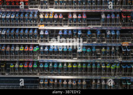 Regal voller farbenfroher Sprühdosen in einem Kunstwarenladen. Strukturierte Zeilen zeigen verschiedene lebendige Farben, die für Graffiti-, Kunst- und Heimwerkerprojekte verwendet werden Stockfoto