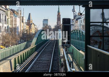 Blick von Berlins U-Bahn-Gleisen in Richtung der Skyline der Stadt mit ikonischer Architektur, einschließlich des Fernsehturms und einer grünen Stahlbahnbrücke. Stockfoto