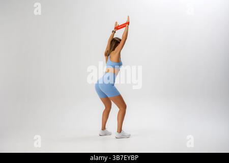 Die Frau führt Widerstandsbandübungen in leichten Trainingsanzügen für Krafttraining durch Stockfoto