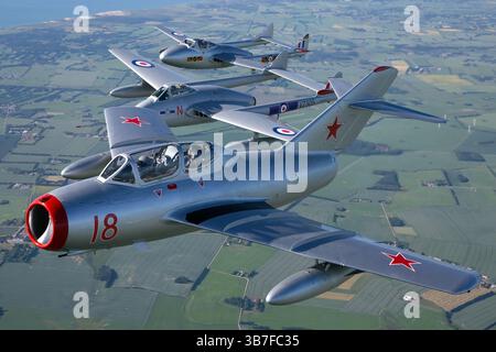 Ein de Havilland DH.100 Vampir (Reg. VZ305) und Mikoyan-Gurevich MiG-15UTI (Reg. 18) der Royal Norwegian Air Force fliegen in Formation. Die DH.100 Vampire ist ein britischer Jet-Jäger, während die MiG-15UTI ein sowjetisches Trainerflugzeug ist, das eine historische Paarung aus der Zeit des Kalten Krieges zeigt. Stockfoto