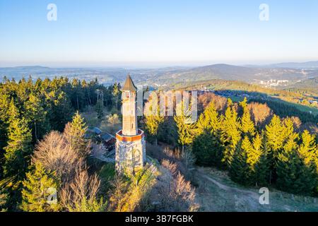 An einem ruhigen Frühlingsmorgen steht der Stepanka Aussichtsturm hoch inmitten üppiger grüner Bäume in Korenov und bietet einen weiten Blick auf das Isergebirge und die umliegende Landschaft. Stockfoto