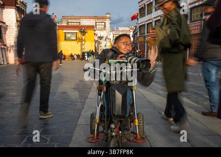 (250506) -- LHASA, 6. Mai 2025 (Xinhua) -- Lhapa Dondrup begrüßt einen Freund, während er Fotos in der Barkhor Street in Lhasa, der autonomen Region Xizang im Südwesten Chinas, am 29. April 2025 macht. Lhapa Dondrup, ein 24-jähriger Mann, der in Lhasa geboren wurde, leidet seit seiner Kindheit an Osteogenesis imperfecta (OI), allgemein bekannt als brüchige Knochenerkrankung. Als Erwachsener steht er unter einem Meter groß und verlässt sich auf Krücken und elektrischen Rollstuhl für Mobilität. Trotz dieser Herausforderungen träumt Lhapa davon, Fotograf zu werden. 2021 trat er einem Kulturmedienunternehmen bei, das von Einzelpersonen wi gegründet wurde Stockfoto