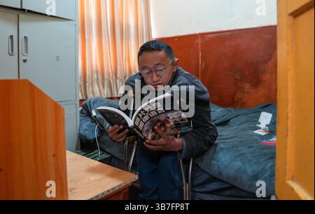 (250506) -- LHASA, 6. Mai 2025 (Xinhua) -- Lhapa Dondrup liest ein Buch über Fotografie im Firmenwohnheim in Lhasa, südwestchinesischer Autonomen Region Xizang, 5. Mai 2025. Lhapa Dondrup, ein 24-jähriger Mann, der in Lhasa geboren wurde, leidet seit seiner Kindheit an Osteogenesis imperfecta (OI), allgemein bekannt als brüchige Knochenerkrankung. Als Erwachsener steht er unter einem Meter groß und verlässt sich auf Krücken und elektrischen Rollstuhl für Mobilität. Trotz dieser Herausforderungen träumt Lhapa davon, Fotograf zu werden. 2021 trat er einem Kulturmedienunternehmen bei, das von Persönlichkeiten mit ph-wert gegründet wurde Stockfoto