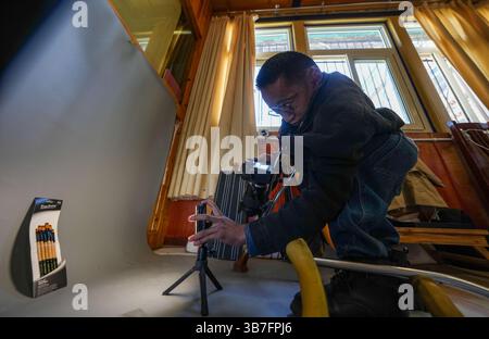 (250506) -- LHASA, 6. Mai 2025 (Xinhua) -- Lhapa Dondrup fotografiert ein Produkt bei der Firma in Lhasa, südwestchinesischer Autonomen Region Xizang, 5. Mai 2025. Lhapa Dondrup, ein 24-jähriger Mann, der in Lhasa geboren wurde, leidet seit seiner Kindheit an Osteogenesis imperfecta (OI), allgemein bekannt als brüchige Knochenerkrankung. Als Erwachsener steht er unter einem Meter groß und verlässt sich auf Krücken und elektrischen Rollstuhl für Mobilität. Trotz dieser Herausforderungen träumt Lhapa davon, Fotograf zu werden. 2021 schloss er sich einem Kulturmedienunternehmen an, das von Menschen mit körperlicher Behinderung gegründet wurde Stockfoto