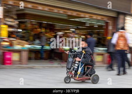 (250506) -- LHASA, 6. Mai 2025 (Xinhua) -- Lhapa Dondrup wird in der Barkhor Street in Lhasa, südwestchinesischer Autonomen Region Xizang, am 29. April 2025 abgebildet. Lhapa Dondrup, ein 24-jähriger Mann, der in Lhasa geboren wurde, leidet seit seiner Kindheit an Osteogenesis imperfecta (OI), allgemein bekannt als brüchige Knochenerkrankung. Als Erwachsener steht er unter einem Meter groß und verlässt sich auf Krücken und elektrischen Rollstuhl für Mobilität. Trotz dieser Herausforderungen träumt Lhapa davon, Fotograf zu werden. 2021 trat er einem Kulturmedienunternehmen bei, das von Menschen mit körperlichen Behinderungen gegründet wurde Stockfoto