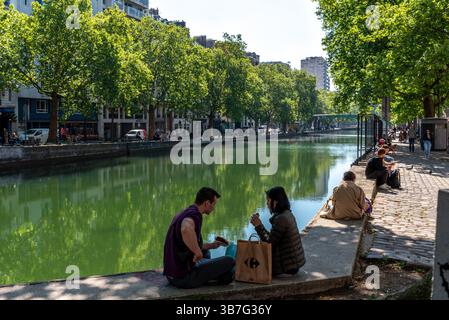 Canal Saint Martin im 10. Arrondissement von Paris. Die Leute essen und genießen das warme, sonnige Wetter am Ufer des Kanals Stockfoto