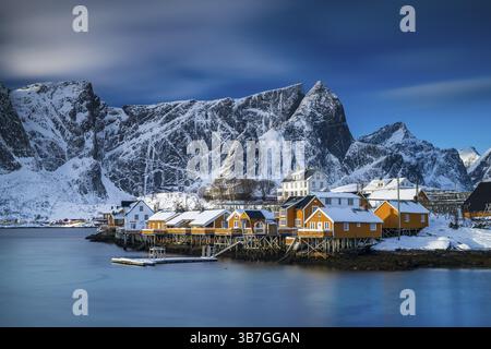 Traditionelle gelbe rorbuer-Hütten auf der Insel Sakrisoy, schneebedeckte Berge im Hintergrund, Sakrisoy, reine, Lofoten, Norwegen, Europa Stockfoto
