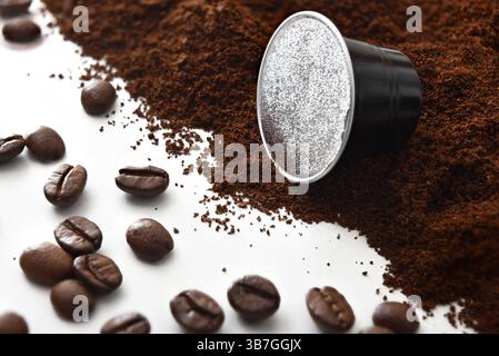 Hintergrund mit Details von schwarzen Espresso-Kapseln auf einem weißen Tisch mit Kaffeebohnen und gemahlenem Kaffee. Erhöhte Aussicht. Stockfoto