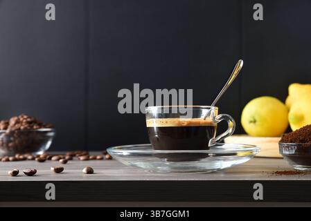 Espresso-Glas-Tasse auf einem Holztisch und Kaffeebohnen um sie herum und ein isolierter schwarzer Hintergrund. Vorderansicht. Stockfoto