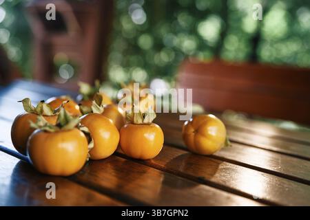 Frisch reife Persimmonen liegen auf einem Holztisch in der Nähe der Bank im Pavillon im Garten. Stockfoto
