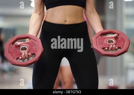 Frau im Fitnessstudio, die zwei rote Hantelplatten hält, während sie in einem Fitnessstudio ein Krafttraining durchführt Stockfoto