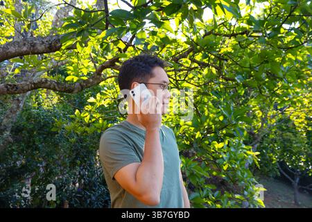 Ein asiatischer Mann benutzt sein Telefon im Grünen, Anruf, SMS oder Videoanruf, Verbindung und Sharing Konzept. Fotomaterial Stockfoto
