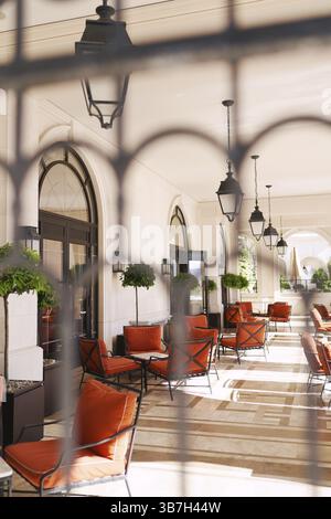 Blick durch das schmiedeeiserne Gitter auf die Hotelterrasse mit weichen Stühlen und Tischen. Stockfoto