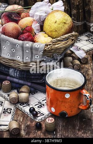 Komposition der Emailtasse mit Wasser auf dem Hintergrund Obstkorb und Lottospiele für Picknick. Foto getönt Stockfoto