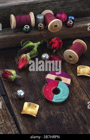 Perlen, Garnspulen auf Vintage-Holzhintergrund mit Rosenknospen verziert Stockfoto