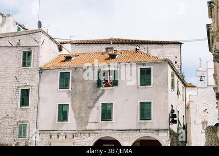 Altes dreistöckiges Wohnhaus mit grünen Fensterläden und orangefarbenen Fliesen auf dem Dach. Stockfoto