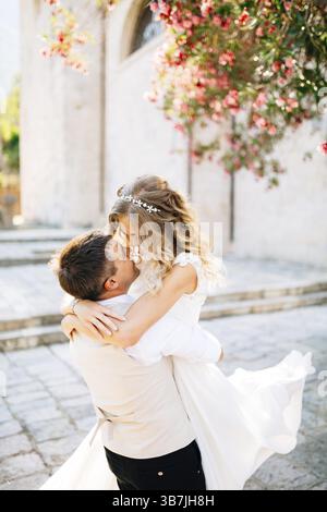 Der Bräutigam hält die Braut in den Armen und küsst auf der Stelle neben der alten Kirche in Prcanj. Stockfoto
