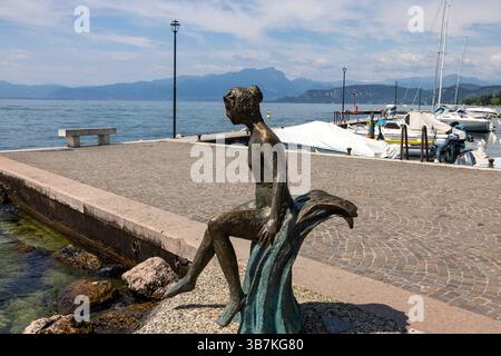 Lazise, Italien - 10. Mai 2024: Die kleine Meerjungfrau (2018), eine Bronzestatue von Libero Cecchini, am Ufer des Gardasees in Lazise. Italien Stockfoto